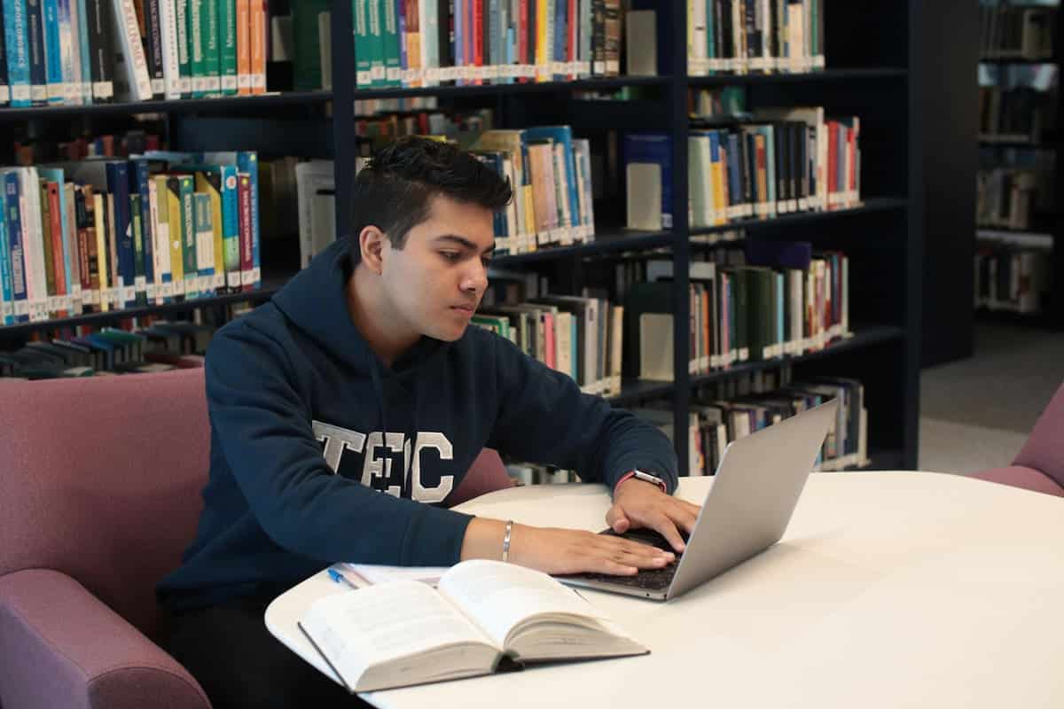 A Student Sitting in a Library and with a Laptop and Studying