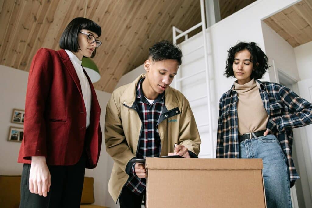 Man Signing Papers on Box Beside Two Women